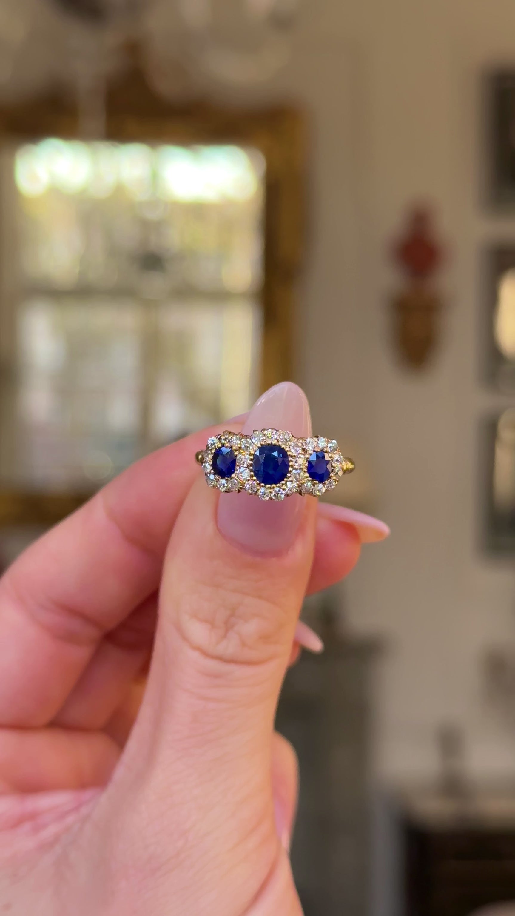 sapphire and diamond triple cluster ring held in fingers and moved around to give perspective.