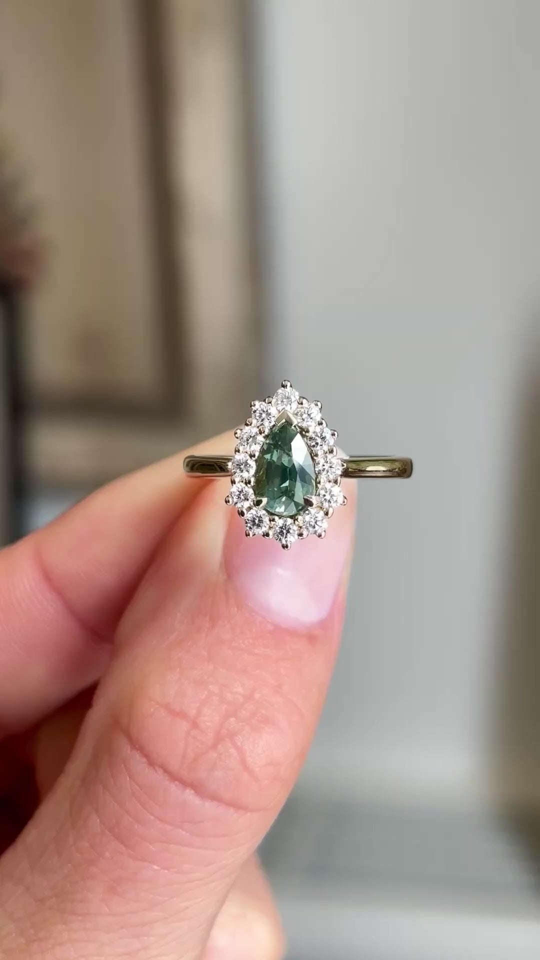 Close-up video of an antique-inspired yellow gold cluster ring featuring a pear-cut green sapphire surrounded by brilliant diamonds, highlighting colour, sparkle and fine detailing against a warm interior setting.