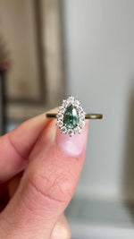 Close-up video of an antique-inspired yellow gold cluster ring featuring a pear-cut green sapphire surrounded by brilliant diamonds, highlighting colour, sparkle and fine detailing against a warm interior setting.