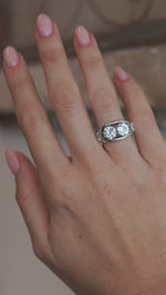 A video of the vintage four-stone diamond ring worn on a finger, capturing the sparkle of the old-cut diamonds and polished white metal setting.