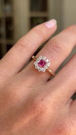 Rectangular step-cut ruby and diamond cluster gold engagement ring featuring a rectangular step-cut ruby surrounded by a halo of diamonds, displayed on a hand.