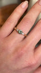 Detailed view of round-cut green sapphire and diamond three-stone engagement ring worn on hand.