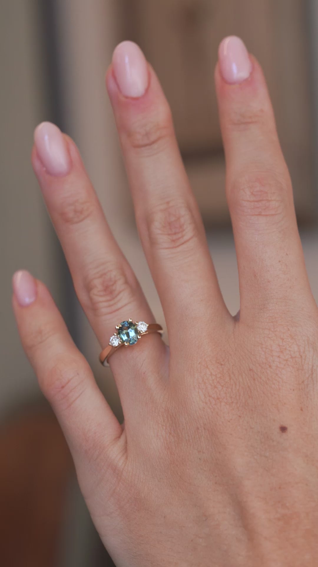 A video of the teal sapphire and diamond ring worn on a finger, capturing the gemstone's changing blue and green tones.