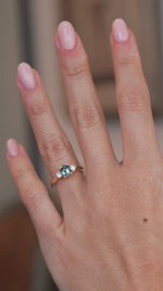 A video of the teal sapphire and diamond ring worn on a finger, capturing the gemstone's changing blue and green tones.