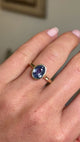 Antique-inspired yellow gold solitaire ring worn on hand, featuring an oval-cut slate blue sapphire in a smooth rub-over setting, filmed against a softly lit vintage interior backdrop.