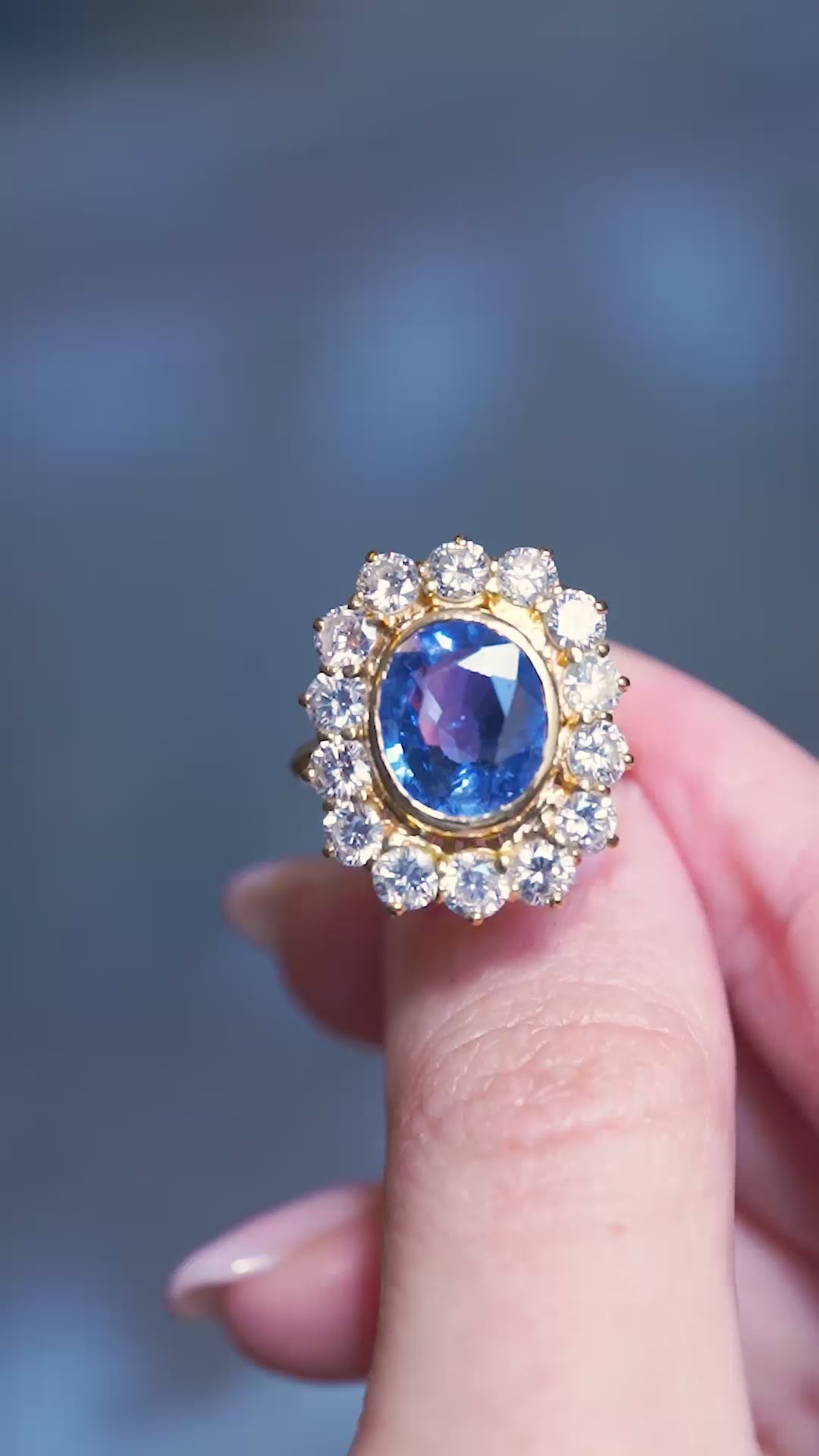 Vintage French sapphire and diamond cluster ring showing a vivid blue centre stone and sparkling diamonds in motion between fingers.