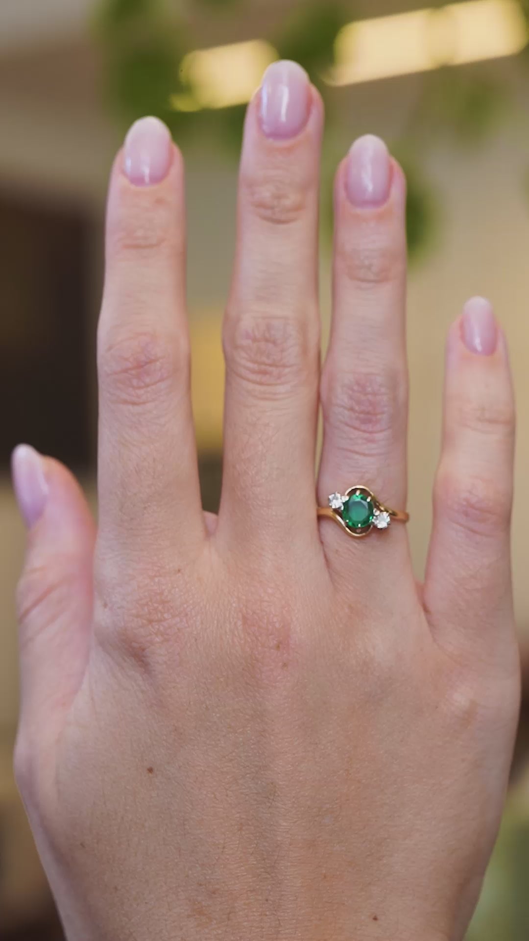 Emerald and diamond three stone ring worn on hand showing rich green tone and natural movement.