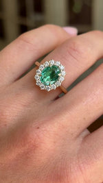 Antique-inspired yellow gold emerald and diamond cluster ring worn on hand, featuring a vibrant oval-cut emerald surrounded by brilliant diamonds, filmed against a softly lit vintage interior backdrop.