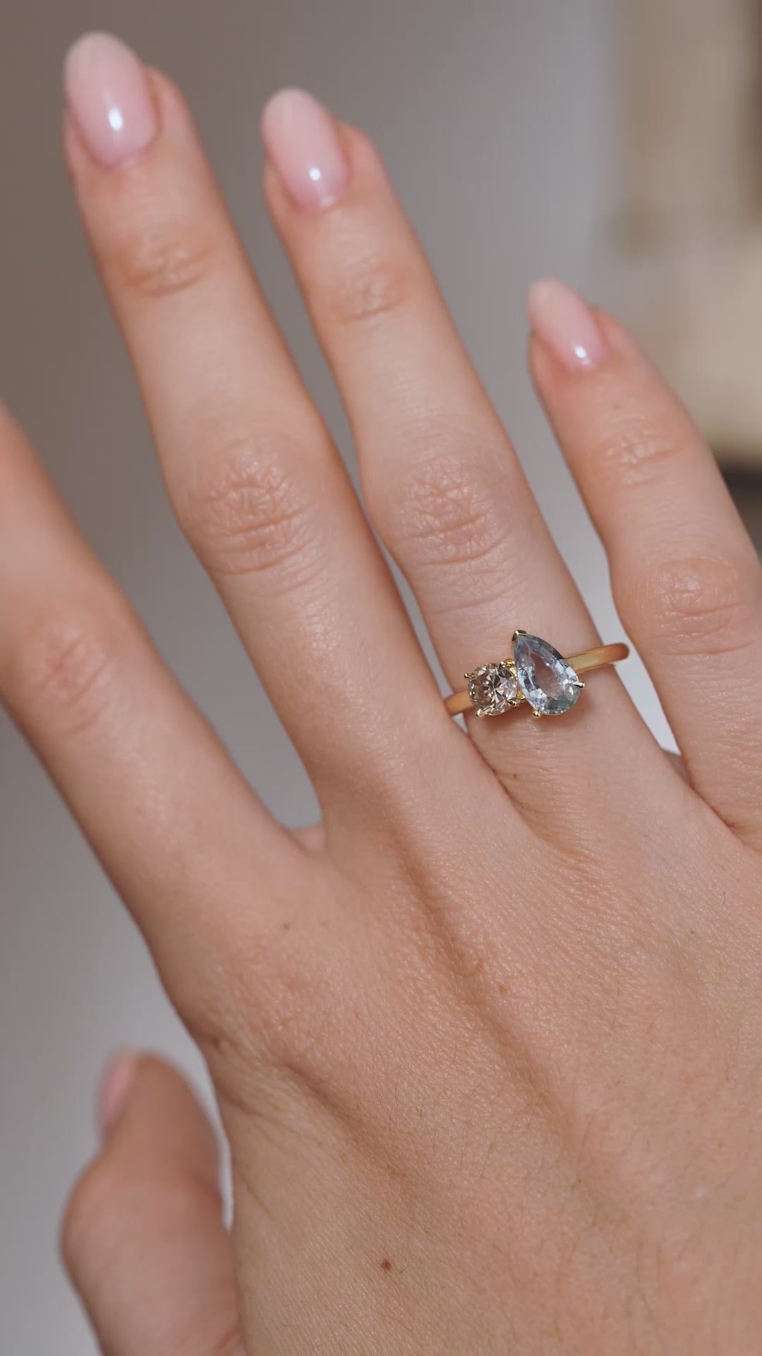 A video of the toi et moi engagement ring worn on a finger, capturing the soft blue sapphire and warm champagne diamond tones.