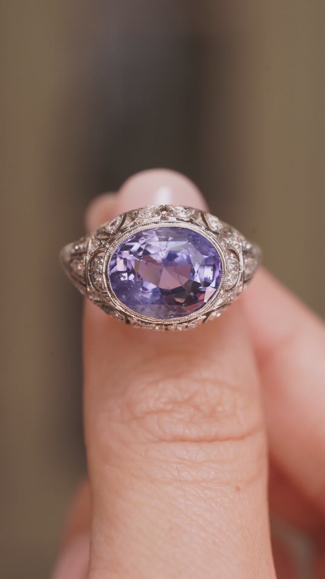 A video of an Antique, Belle Époque Ceylon colour-change sapphire and diamond cluster ring in platinum held between the fingers and rotated to show angles