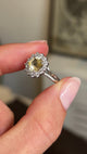 Close up video of a platinum Antique inspired, yellow sapphire and diamond cluster engagement ring held between two fingers and rotated to showcase the central sapphire
