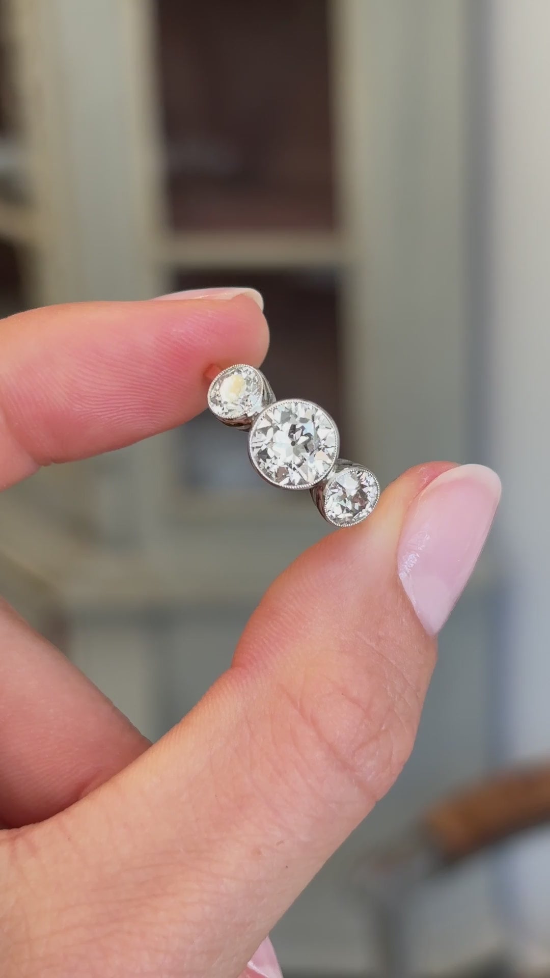 Antique Edwardian old-cut diamond three-stone engagement ring featuring three old-cut diamonds in a timeless trilogy design, held by hand for detailed viewing.