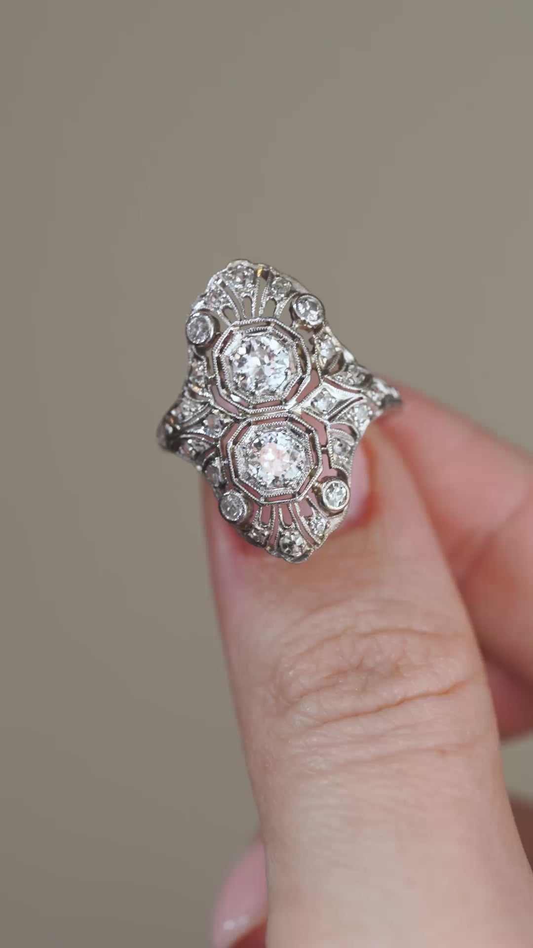 A video showing the diamond cluster cocktail ring held between fingers, capturing its elaborate filigree metalwork and distinctive Art Deco silhouette.