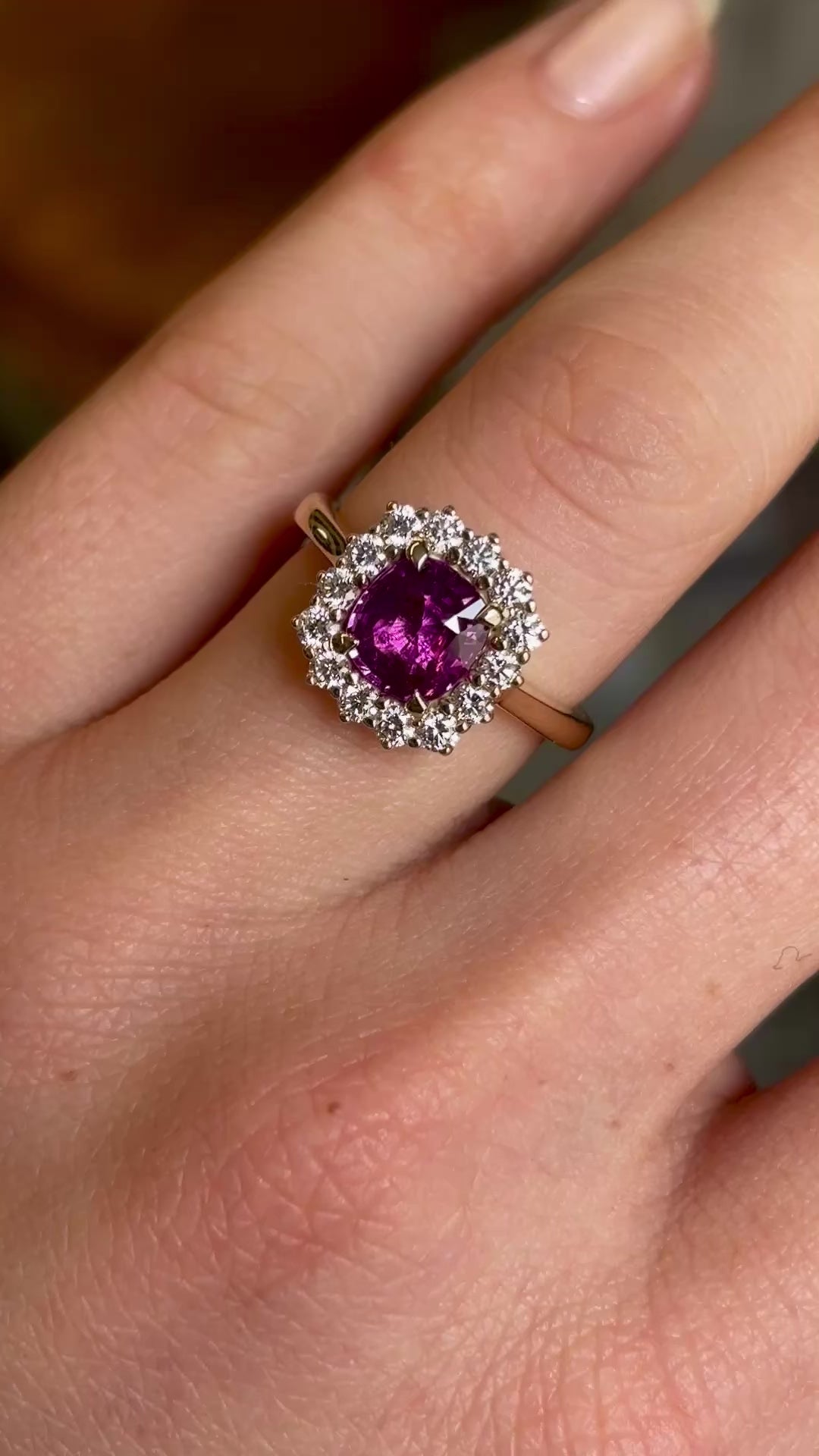 Square-cut pink sapphire and diamond cluster engagement ring worn on the ring finger of the left hand close up and slowly moving back
