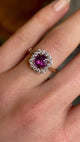 Square-cut pink sapphire and diamond cluster engagement ring worn on the ring finger of the left hand close up and slowly moving back
