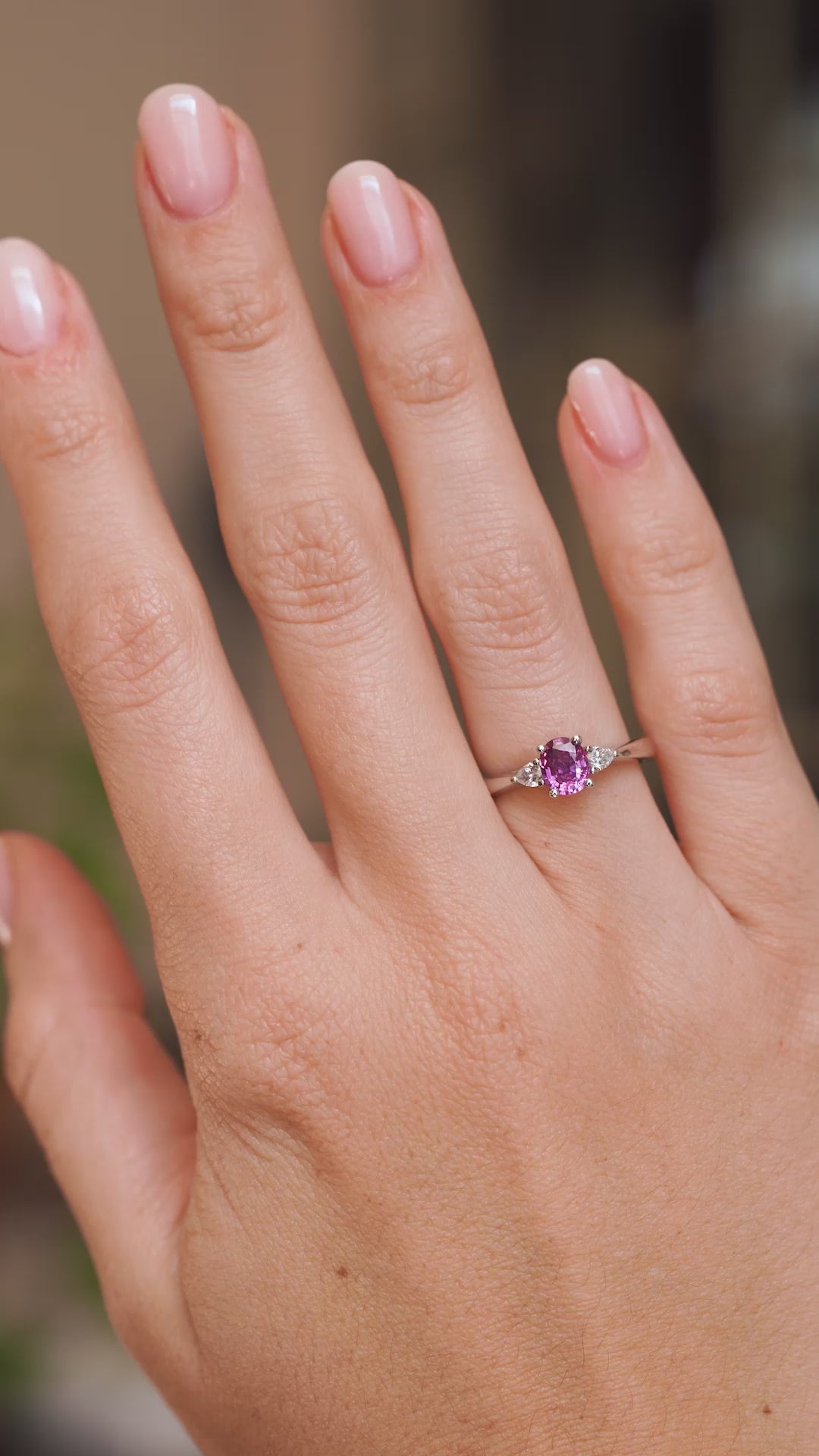 Video of a purple-pink sapphire three-stone ring worn on the hand, highlighting the central gemstone and pear-cut diamond sides.