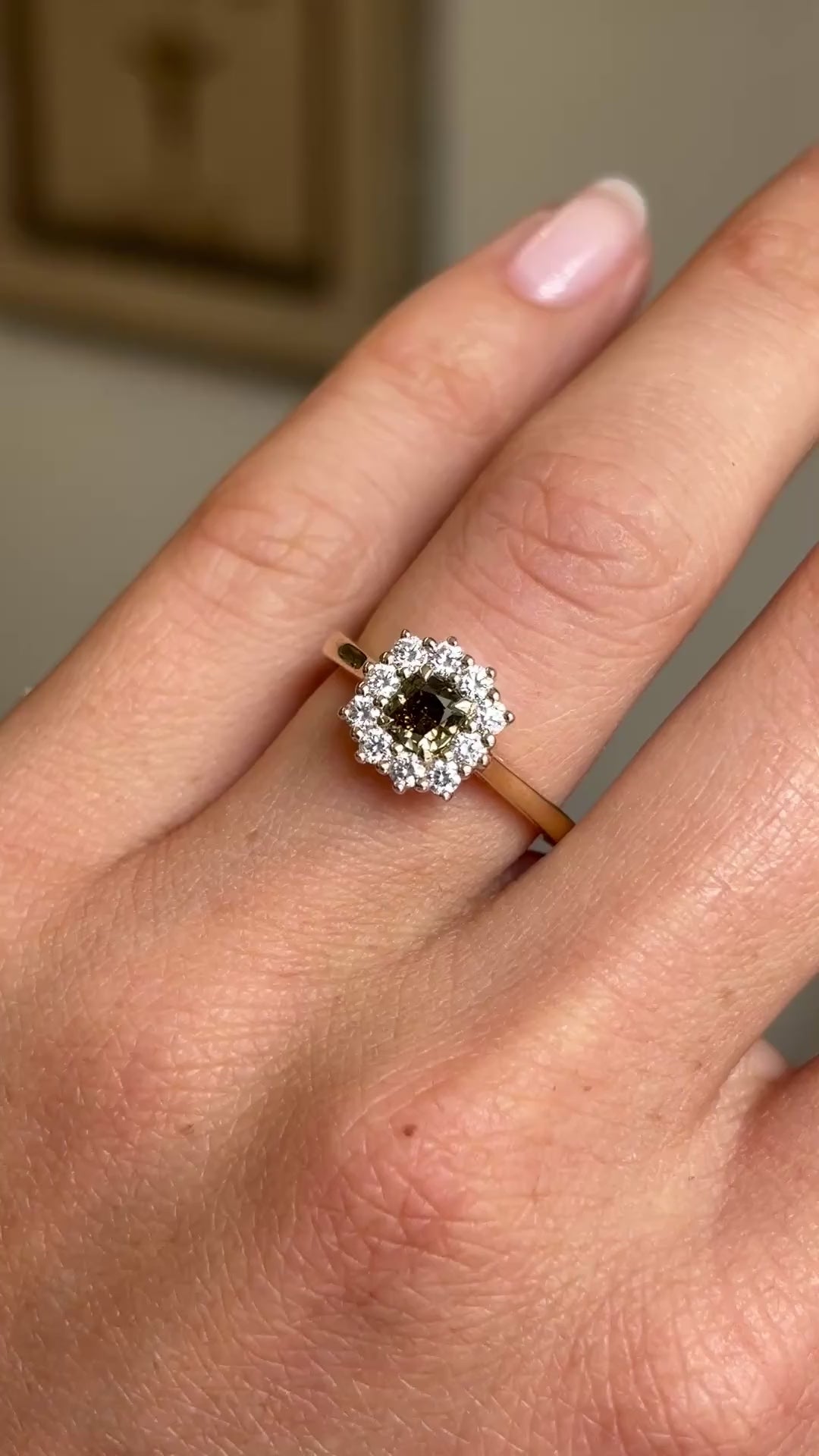 A close-up video of an Antique-inspired, Brown diamond cluster engagement ring, set with a central square-cut brown diamond surrounded by a halo of round brilliant-cut diamonds, worn on a wedding finger. 