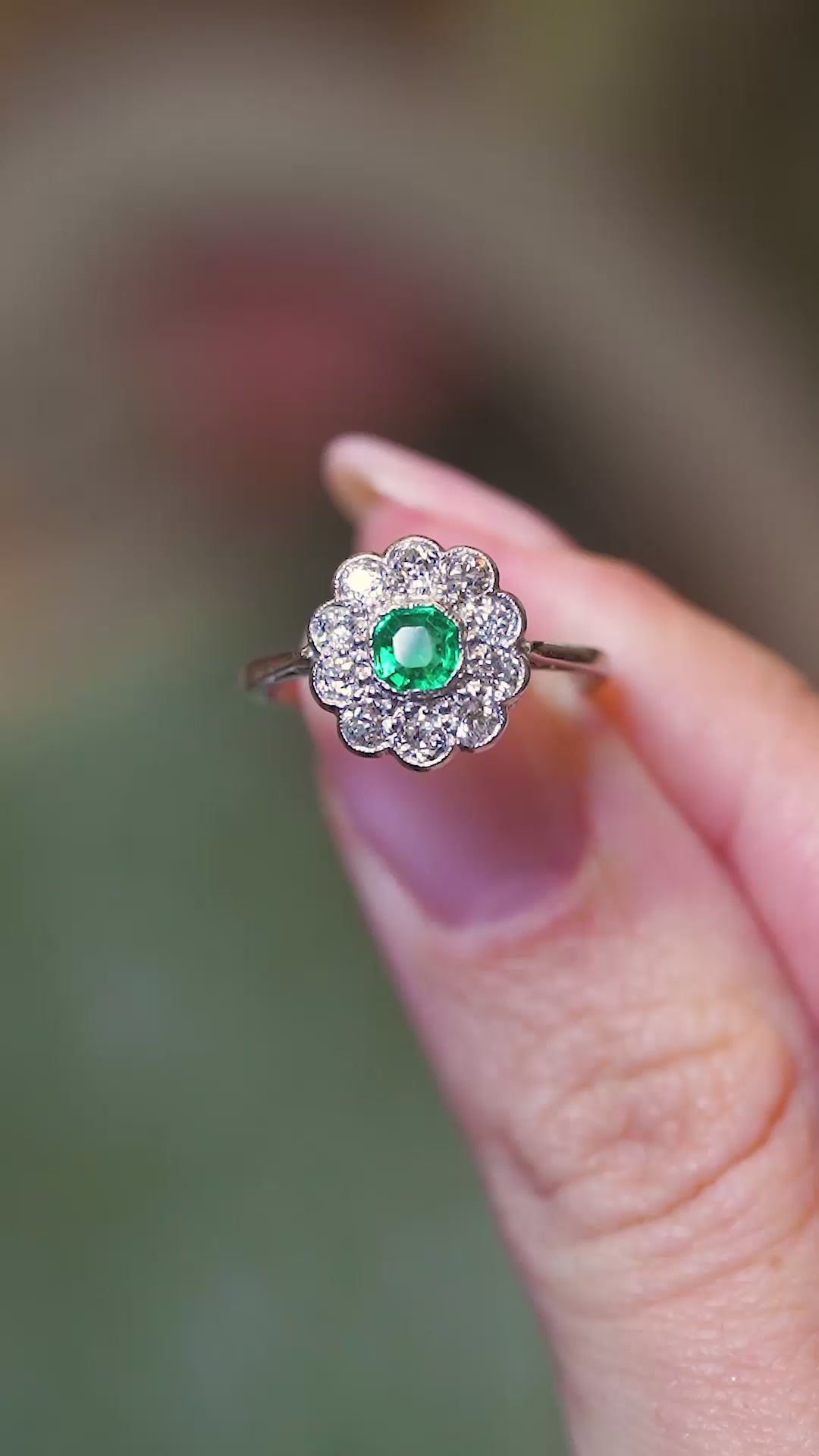 Antique Edwardian emerald and old-mine cut diamond cluster ring shown in subtle movement between fingers.