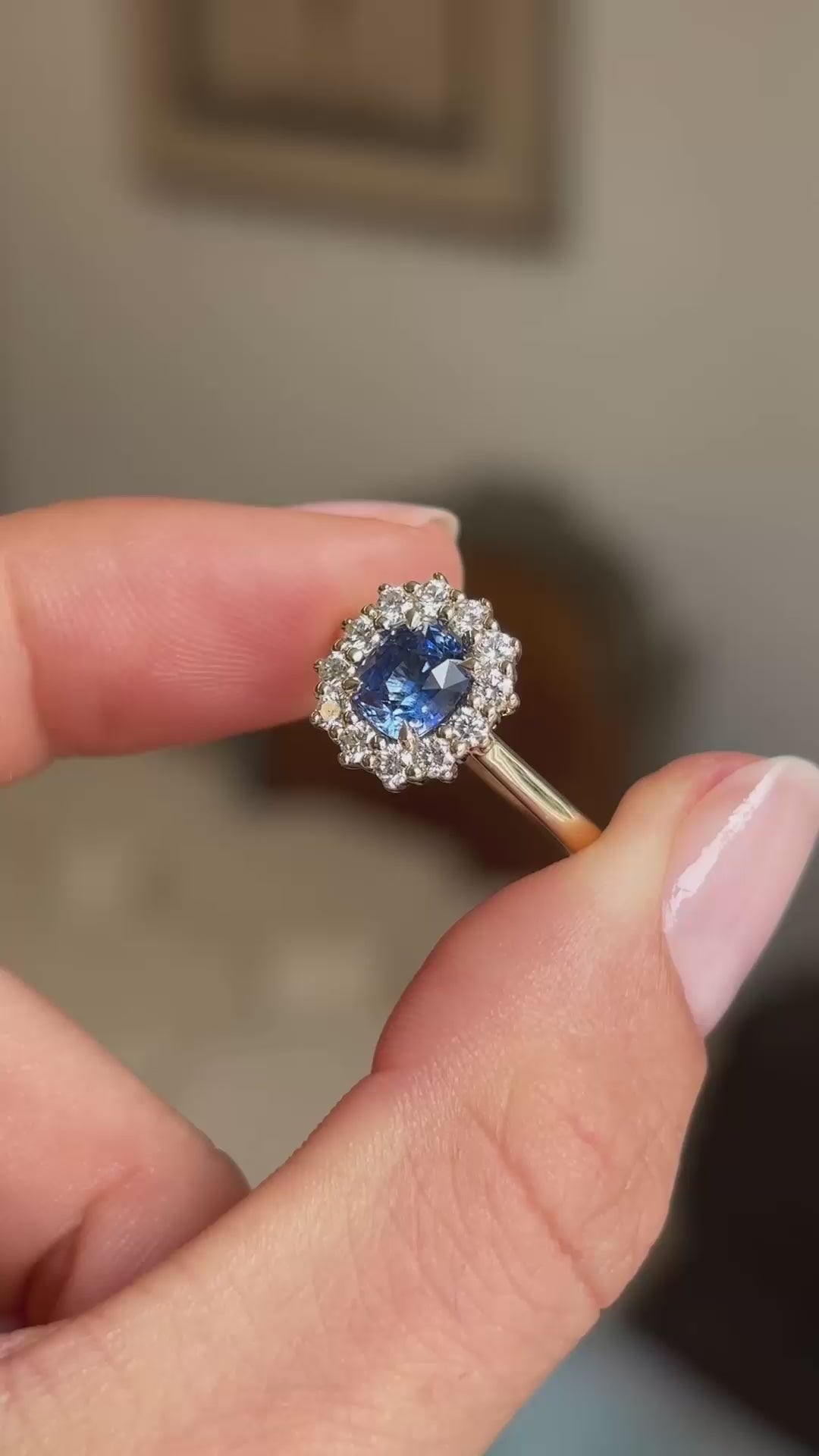 A video close-up of a blue sapphire and diamond halo engagement ring held between fingers.