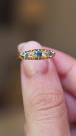 A close-up detail of a video of an antique Edwardian blue sapphire and diamond five-stone ring held between the fingers.