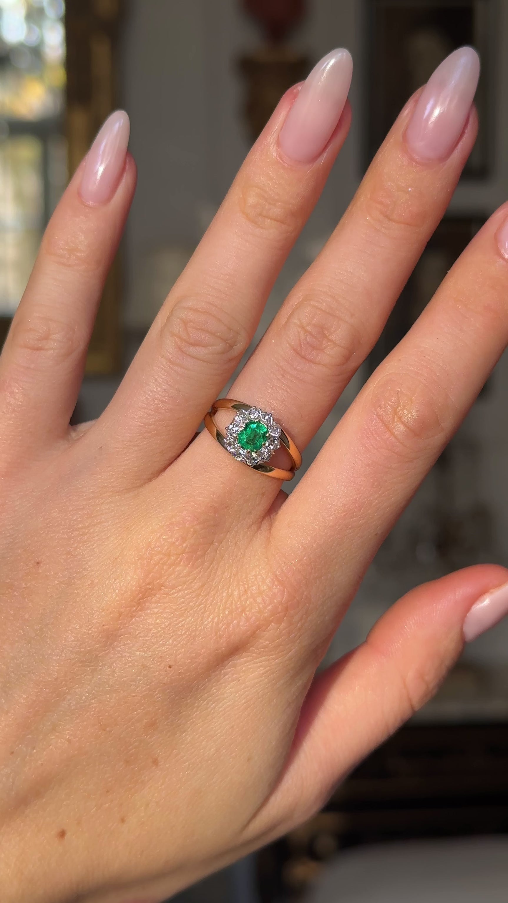 Vintage emerald and diamond cluster ring on hand moved away from camera to give perspective. 