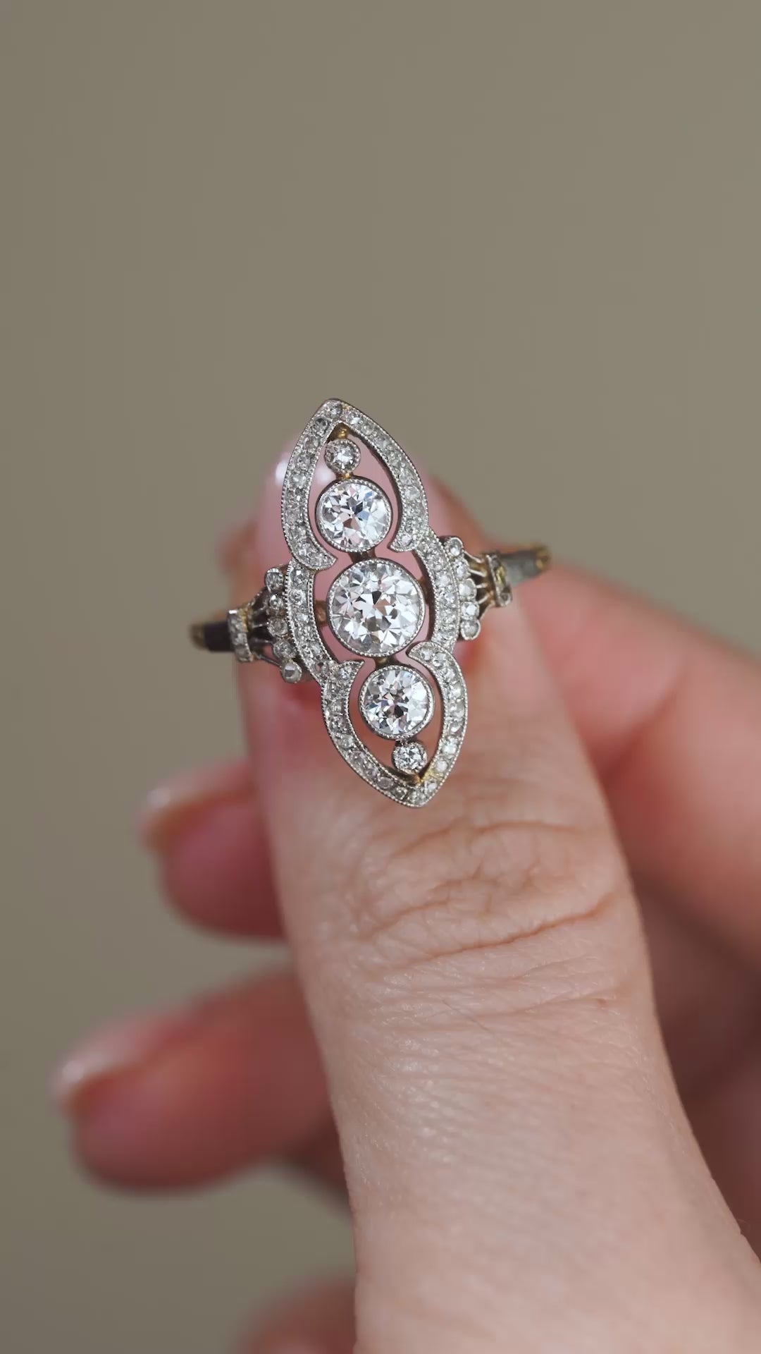 A close-up video of the antique diamond cluster ring held between fingers, capturing the sparkle of its old-cut diamonds and ornate openwork design.