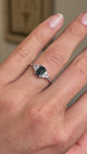 A video of a vintage-inspired engagement ring with a green sapphire at the centre, flanked by a diamond cluster trefoil on both shoulders. 