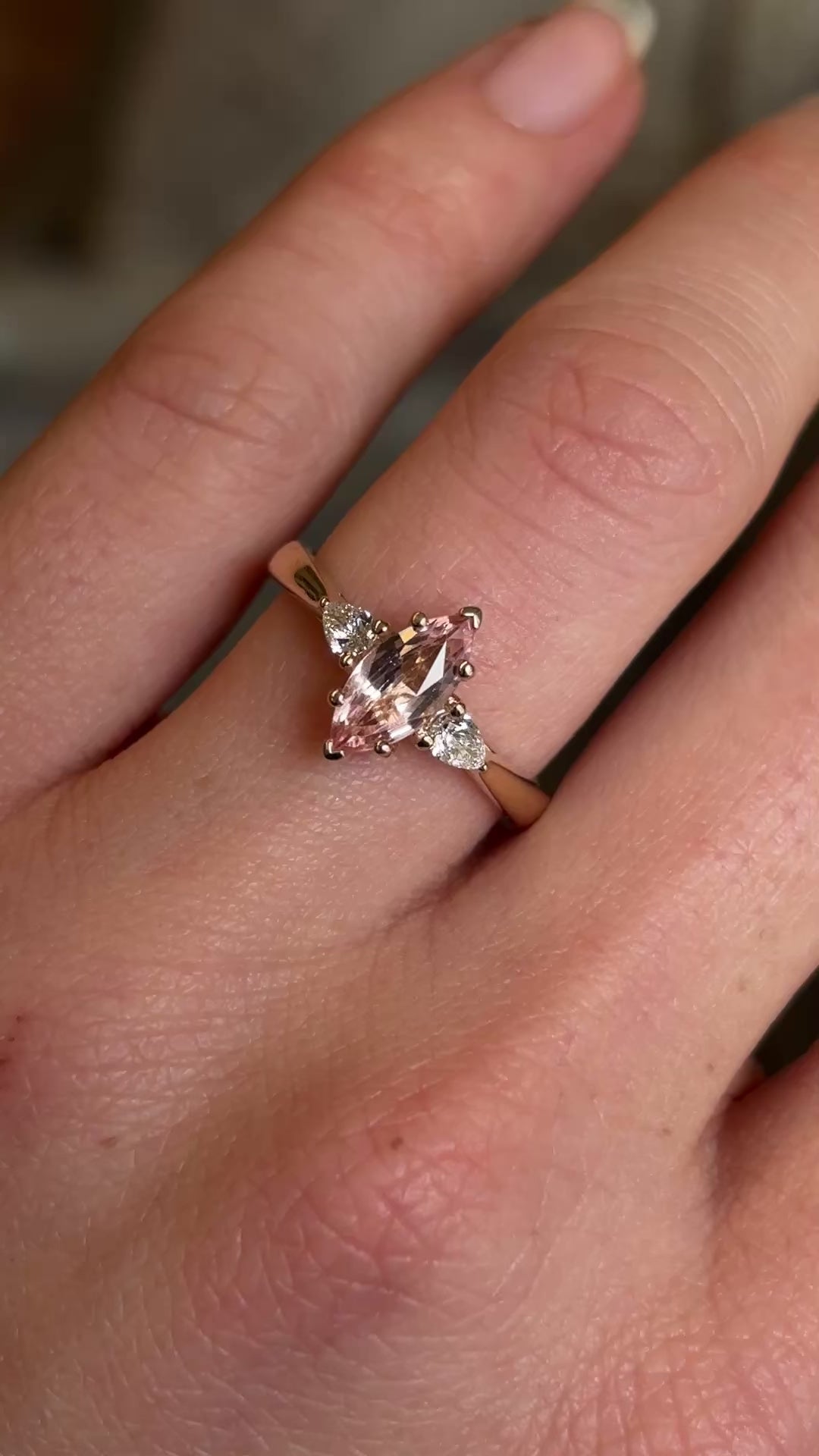 Pink Marquise-cut sapphire and diamond three-stone engagement ring on hand at a distance to show scale. 