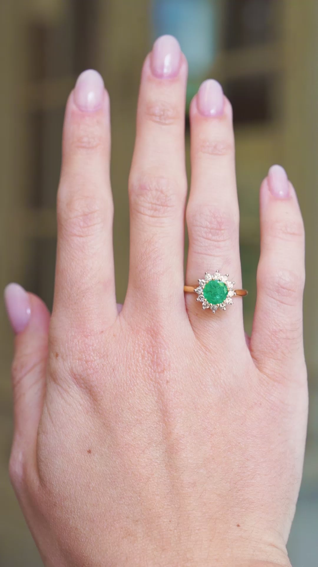 Vintage emerald ring worn on hand with diamond surround showing natural movement.