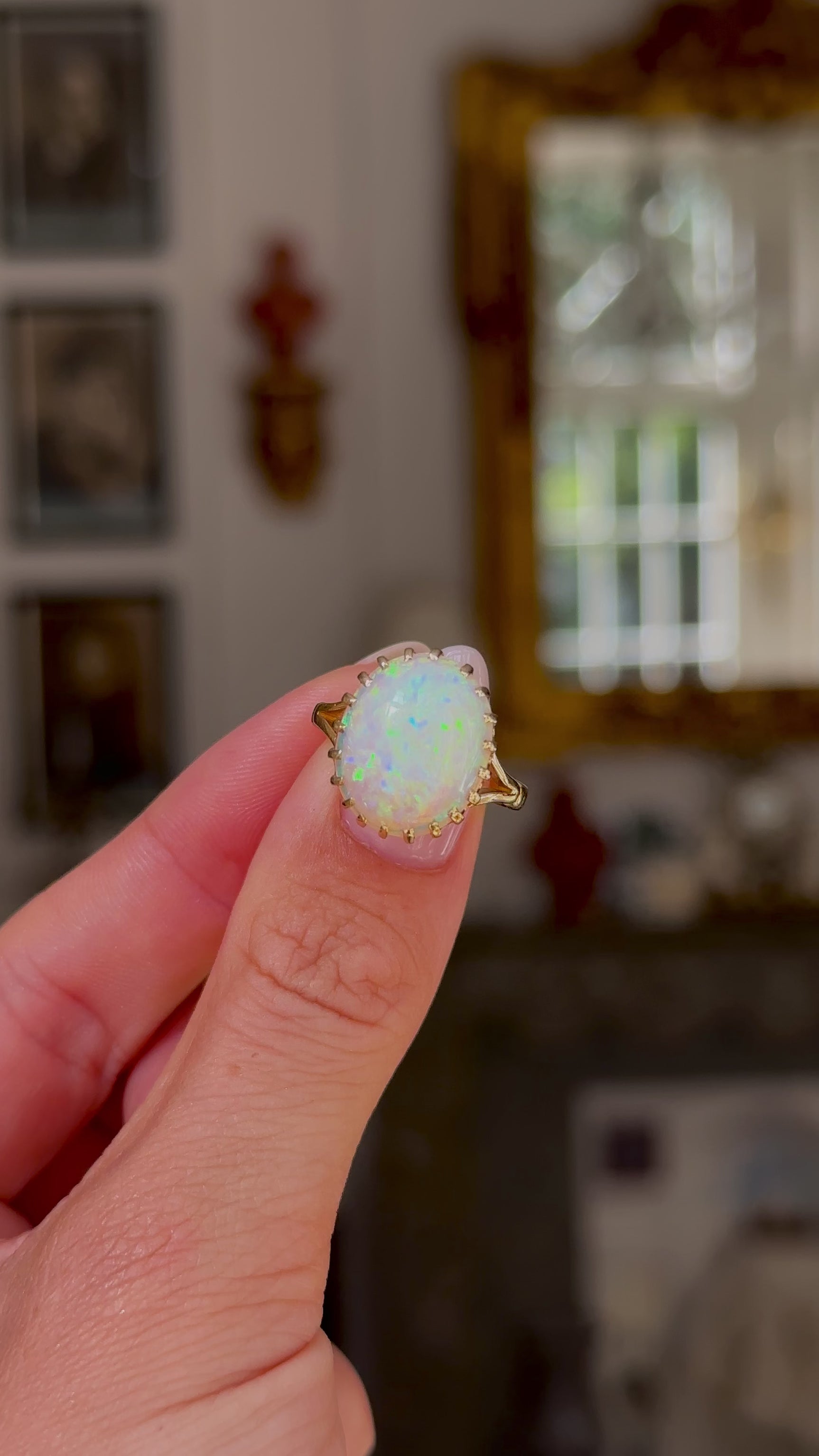 cabochon white opal cocktail ring with 18ct yellow gold band, held in fingers and rotated to give perspective, front view. 