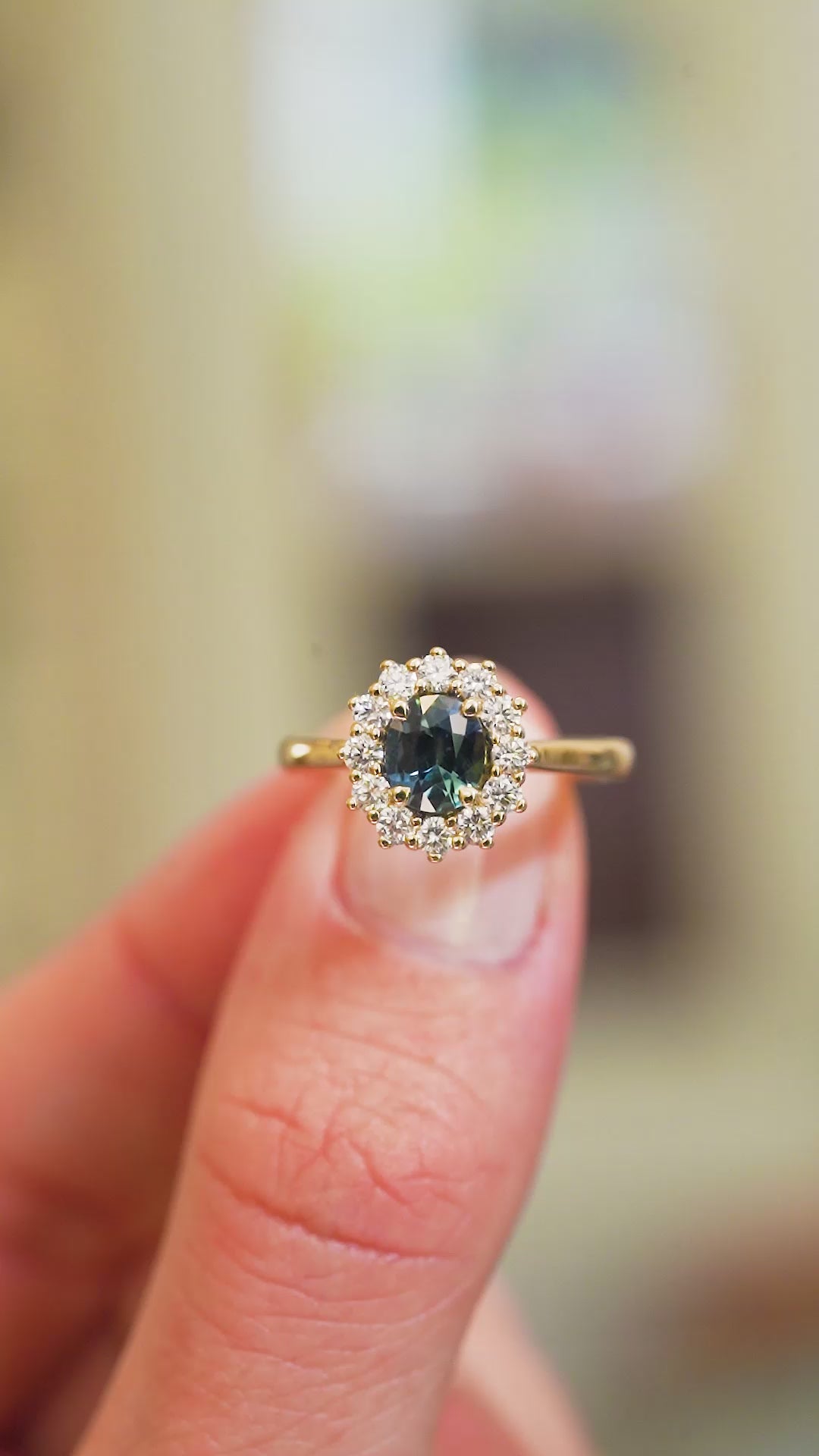 Oval cut teal sapphire ring with diamond halo showing light reflections and gemstone detail.