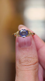 A video of a close detail of a vintage-inspired blue sapphire engagement ring with diamond accents in yellow gold shown between two fingers.