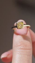 A close-up video of the antique-inspired yellow sapphire solitaire held between fingers, revealing the gemstone's natural facets and square gold setting.