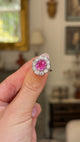 Pink sapphire and diamond cluster ring held in fingers and moved around to give perspective.