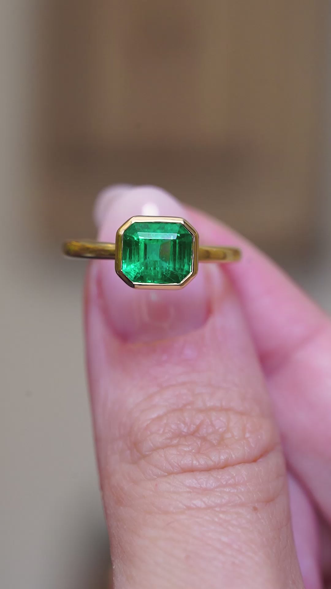 A video of an antique-inspired emerald-cut emerald solitaire engagement ring held between the fingers.