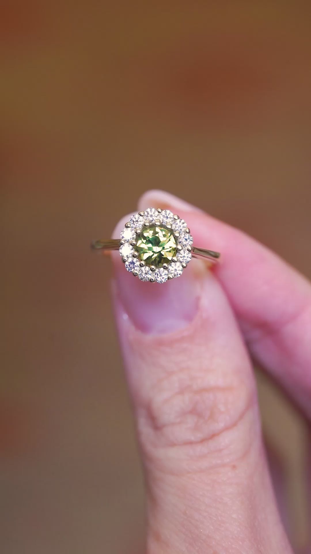 Green sapphire and diamond cluster engagement ring shown in motion between fingers.