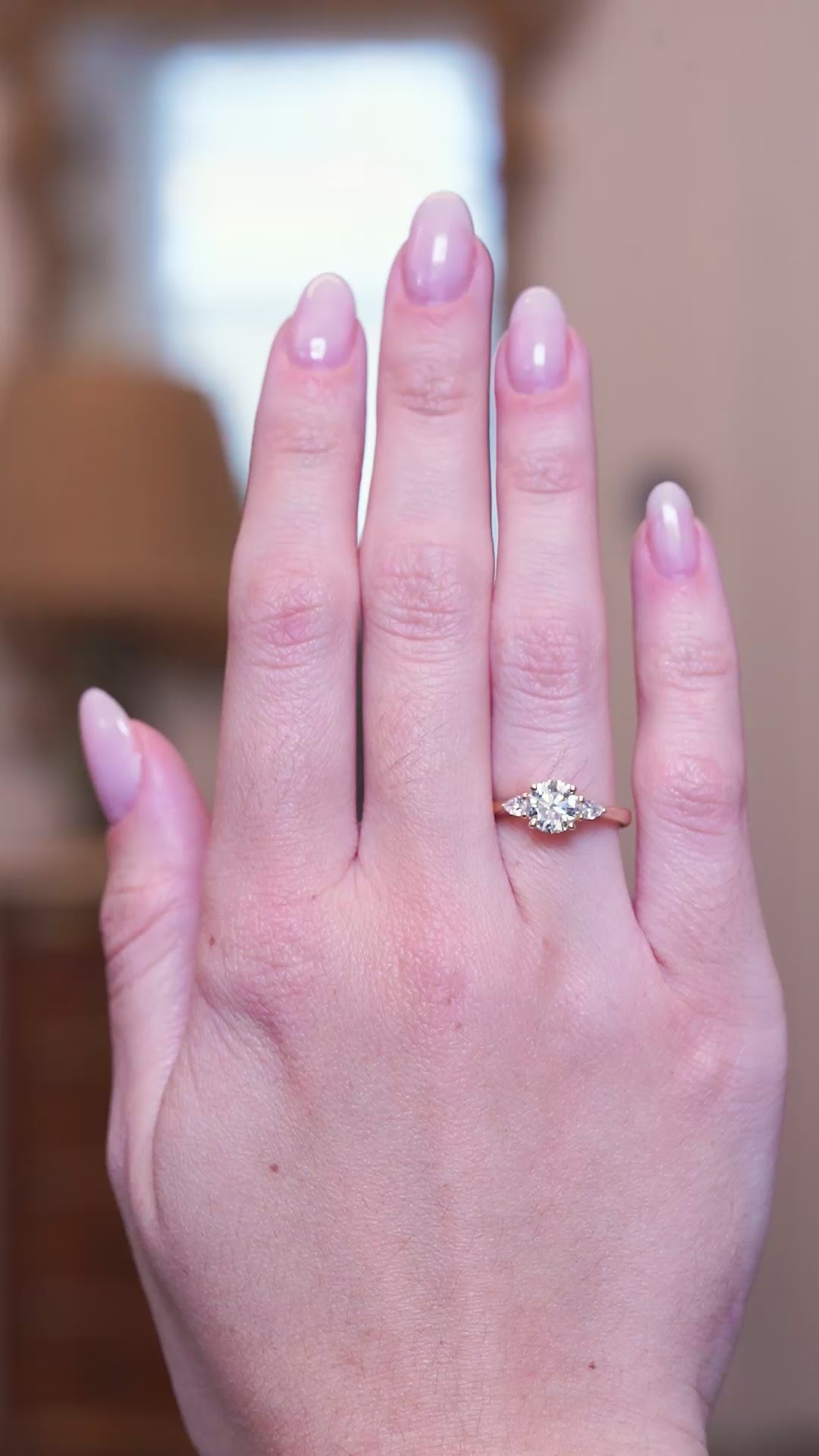 Round brilliant-cut diamond three-stone engagement ring worn on hand shown in subtle motion.
