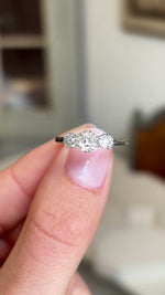 A close up video of a Vintage, 1940s white gold engagement ring.  Held between two fingers and rotated slowly to showcase the white gold band and the three old-cut diamonds. 