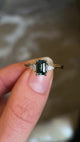 Green sapphire and diamond three-stone engagement ring held in fingers and rotated to show details