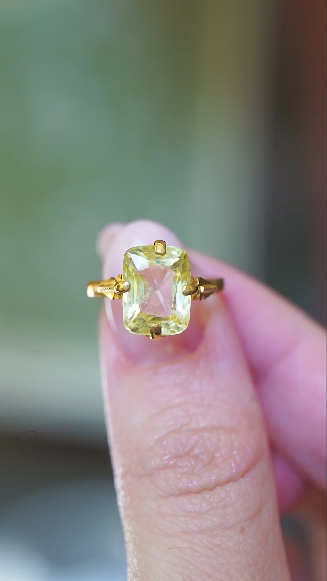 Detailed view of antique Victorian yellow sapphire solitaire ring showing ornate gold setting between fingers.