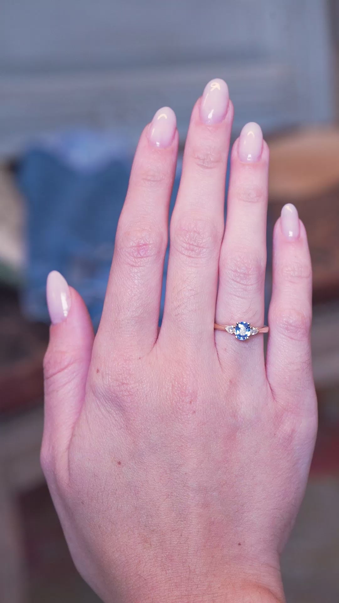 Light blue sapphire and diamond three-stone engagement ring worn on hand with subtle movements.