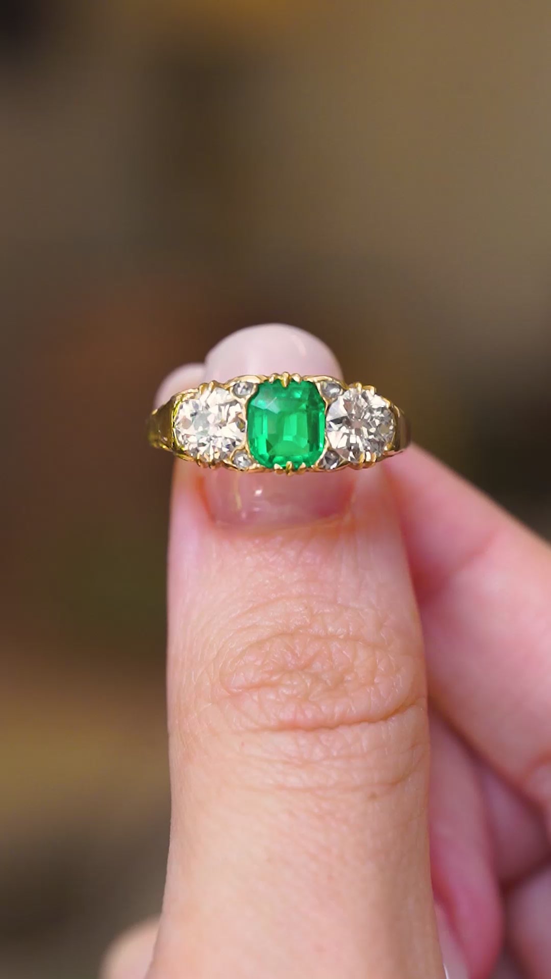 An antique, Victorian green emerald and diamond three-stone ring shown in video held between fingers.