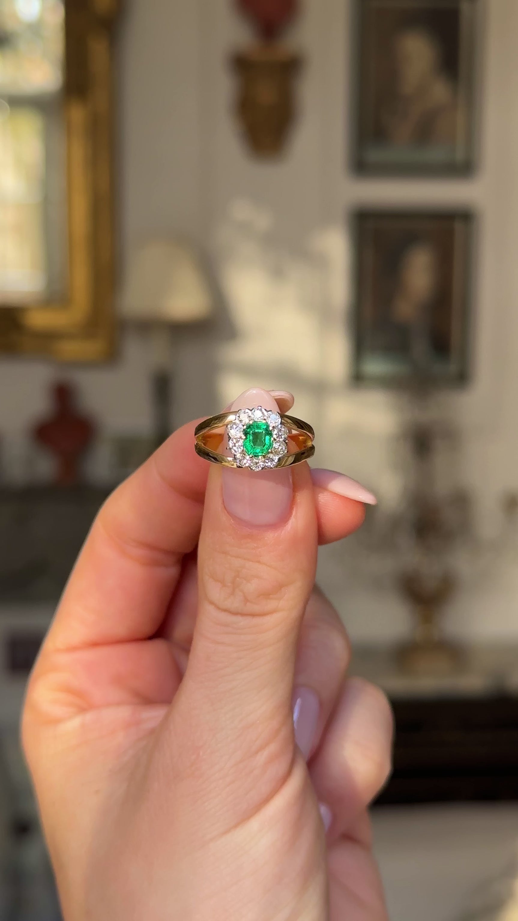 Vintage emerald and diamond cluster ring in fingers moved away from camera to give perspective. 