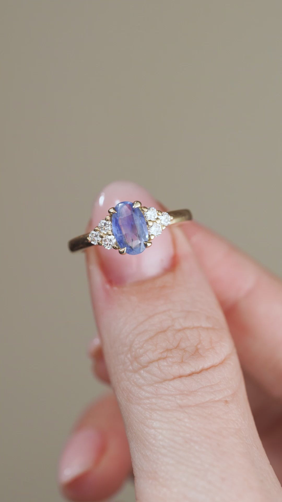 A video showcasing the yellow gold sapphire and diamond ring held between fingertips, capturing the gemstone's soft blue tones and sparkle.