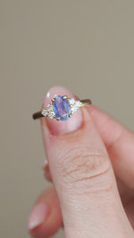 A video showcasing the yellow gold sapphire and diamond ring held between fingertips, capturing the gemstone's soft blue tones and sparkle.
