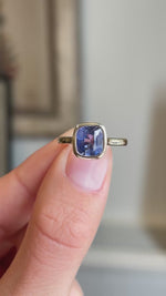 An antique-inspired, violet-blue sapphire solitaire engagement ring in yellow gold held between fingers in a video.