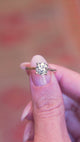 Cushion old-mine cut diamond solitaire engagement ring held between fingers showing ring details in motion.