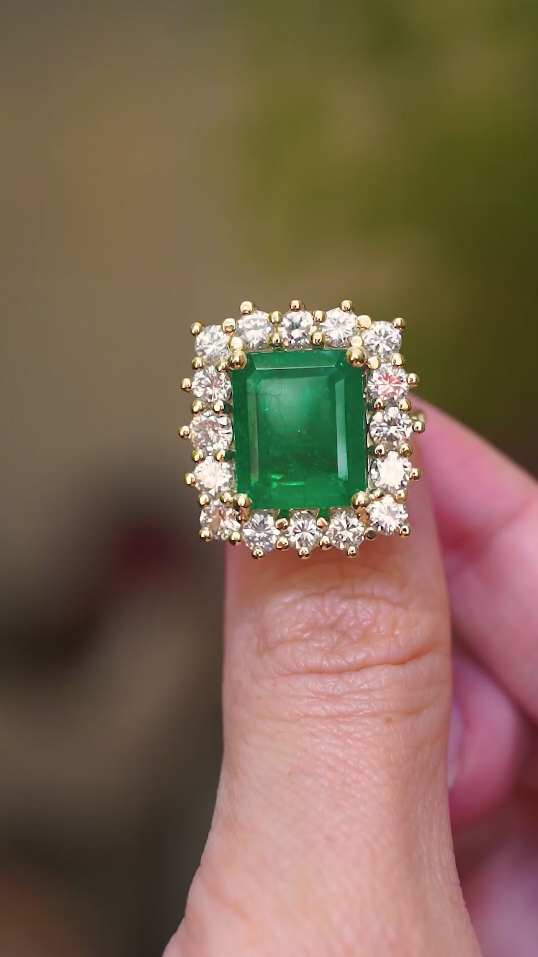 A vintage inspired emerald and diamond halo ring, shown in a video held between fingers displaying varied angles.