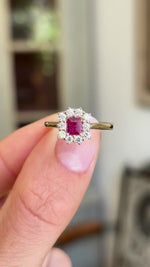 Rectangular step-cut ruby and diamond cluster gold engagement ring showcasing a rectangular step-cut ruby and diamond halo, held by hand to highlight the setting and craftsmanship.