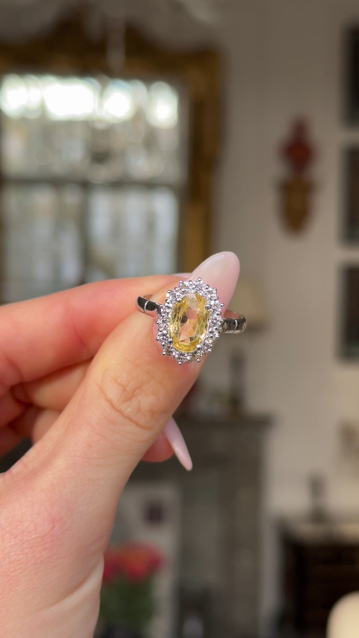 Yellow sapphire and diamond cluster engagement ring, held in fingers and rotated to give perspective.